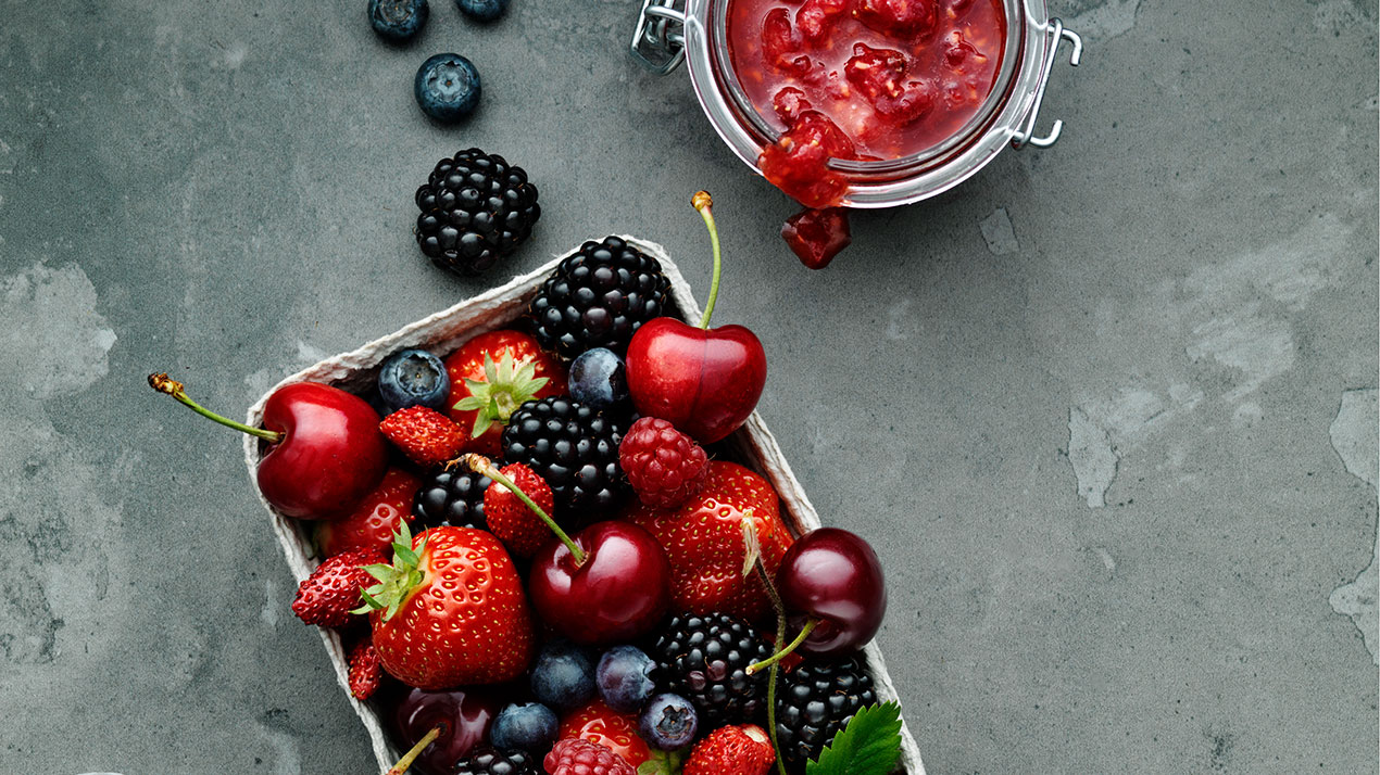 En burk bärkompott och en pappform fylld med björnbär, blåbär, körsbär, jordgubbar och hallon.Symboliserar sötma.