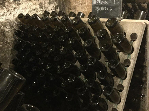 Cavaflaskor uppställda med korken nedåt i träställ i en källare.
