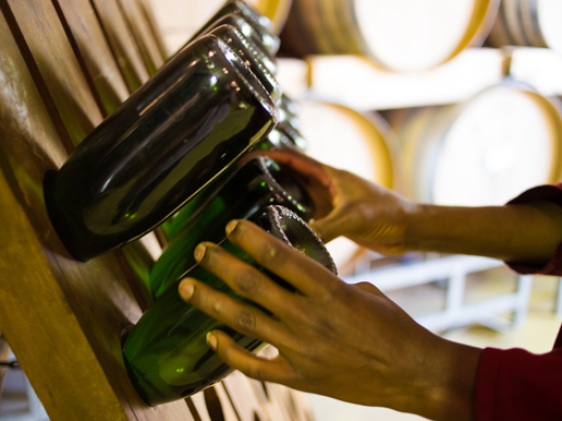 Två händer som snurrar flaskor med mousserande vin i en träställning. 